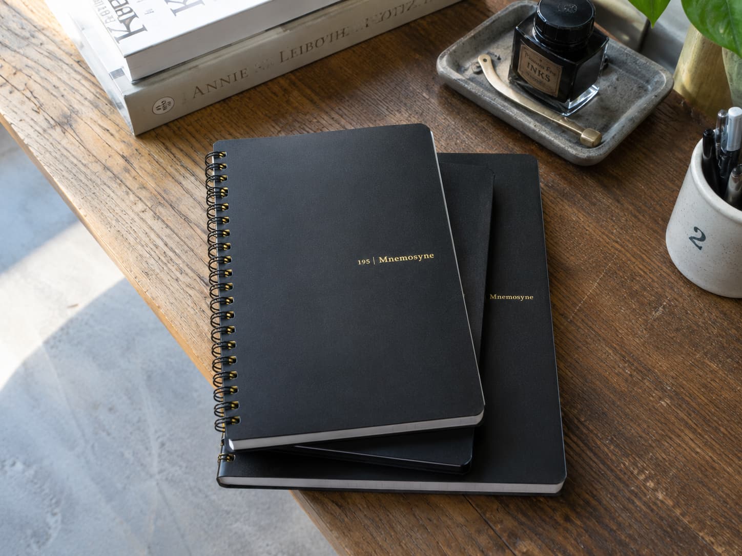 Black Maruman Mnemosyne spiral notebooks on a wooden desk with ink and pens
