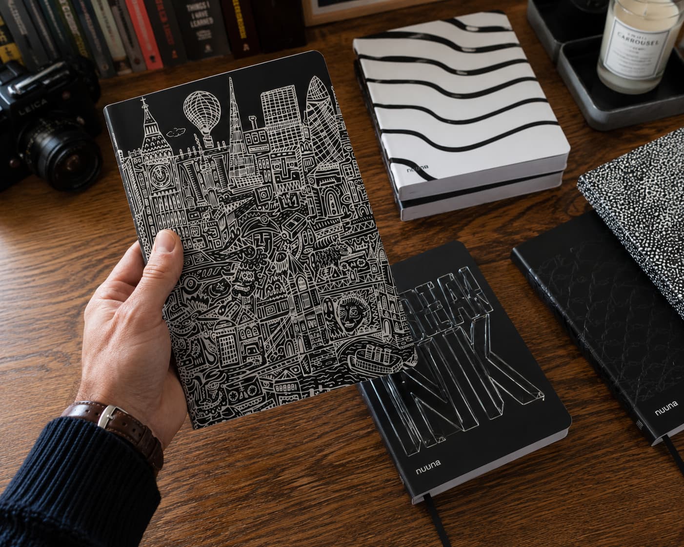Nuuna graphic notebooks on a wooden desk with a camera, candle, and books